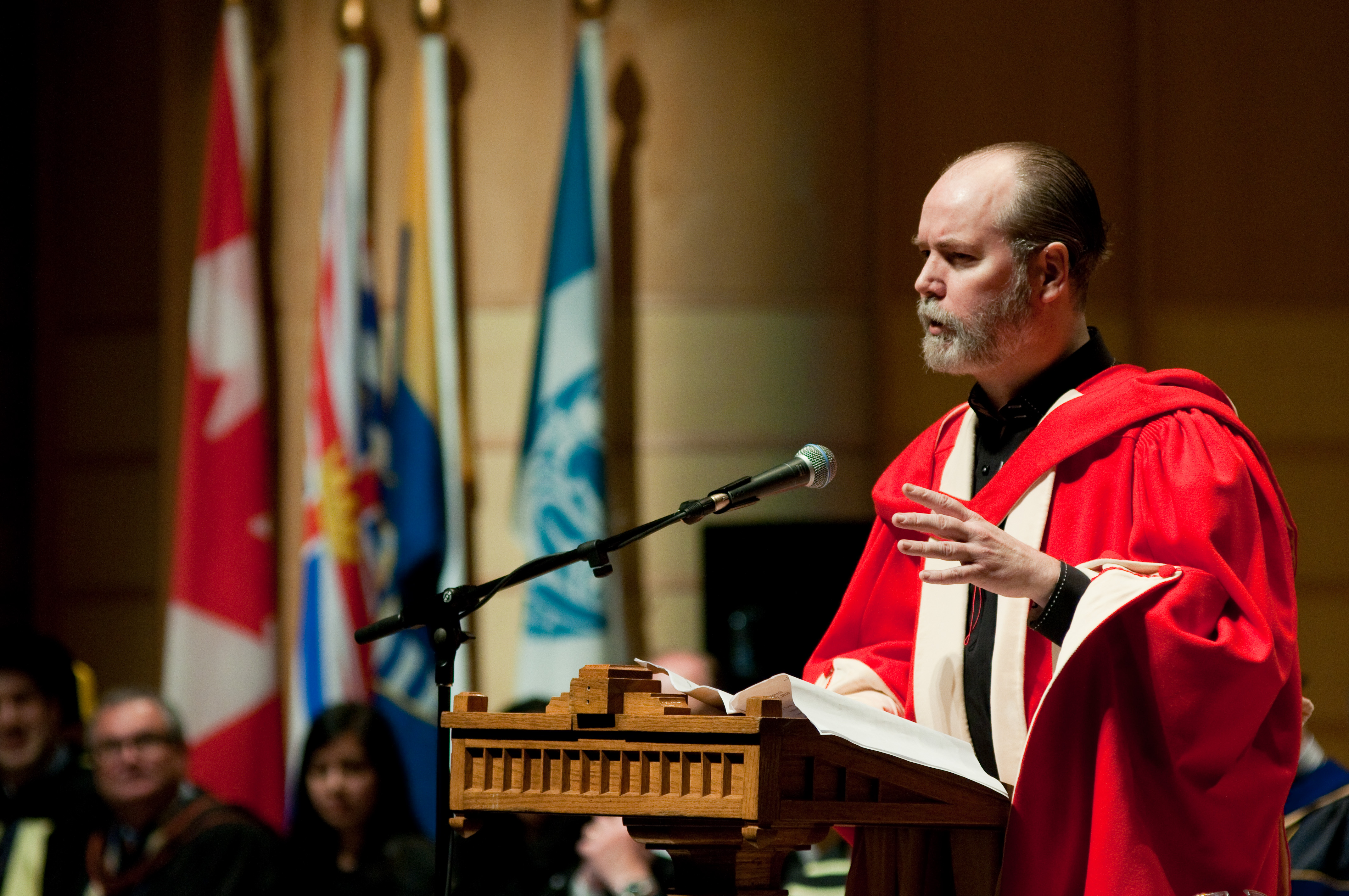 Douglas Coupland speaking at a podium at his honorary degree ceremony.