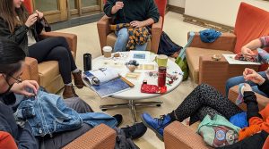 People engage in crafting activities around a small table in a room with armchairs.