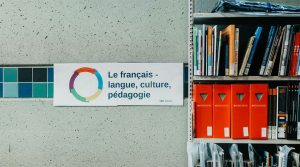 A library sign reads "Le français - langue, culture, pédagogie" next to a shelf filled with books and orange magazine holders.